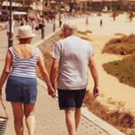 Photo by Sam Williams for Unsplash. Two older people walking together in short sleeves and shorts.